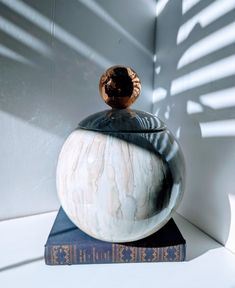 a white vase sitting on top of a book next to a shadow cast wall behind it