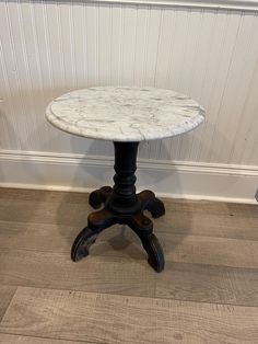 a small white marble topped table sitting on top of a hard wood floor next to a wall