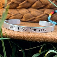 "Aluminum cuff bracelet, hand stamped with the words \"Long Live Cowgirls\"  This lightweight, adjustable bracelet is made from aluminum. This means the bracelet is hypoallergenic, tarnish and rust resistant, and will not turn your skin green. It can be worn in water, but know that the ink inside the stamps may fade over time due to too much exposure to water or chemicals. Avoid bending the metal too much, as this will weaken it and can lead to damage or breaks. I hand stamp every accessory and piece of jewelry myself, so every piece is unique. Please allow for some discrepancies as I can not make any two items identical. Each character is stamped individually. This means that alignment and spacing may vary.  Please contact me if you have any questions and I will be happy to answer them!" Western Style Turquoise Stamped Bracelets, Stamped Bracelet Western, Western Stamped Jewelry, Western Metal Stamped Jewelry, Western Style Stamped Turquoise Cuff Bracelet, Western Turquoise Stamped Cuff Bracelet, Western Cuff Bracelet, Cowgirl Bracelets, Long Live