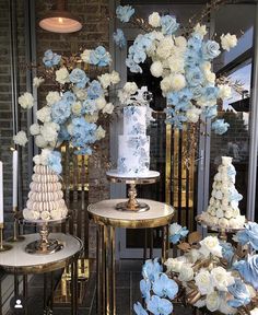 blue and white flowers are on display in front of a storefront with gold pedestals