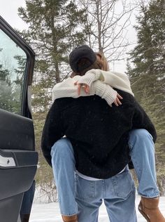 a man and woman hugging in front of a car with snow on the ground behind them