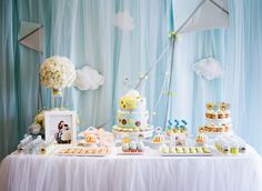 a table topped with lots of cakes and cupcakes next to a wall covered in clouds