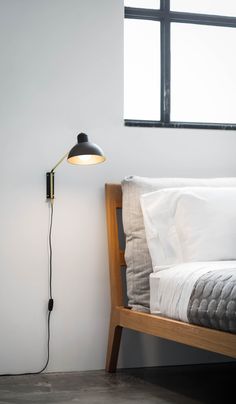 a bed with white sheets and pillows next to a black lamp on the side of it