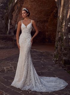 a woman in a wedding dress standing on a cobblestone walkway with an archway behind her