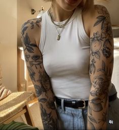 a woman with tattoos on her arms and chest standing in front of a bed, looking at the camera