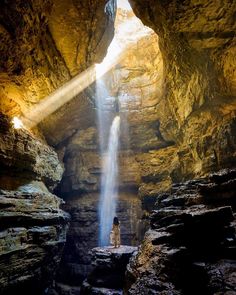 a person standing in the middle of a cave with a waterfall coming out of it