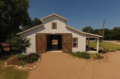 a white barn with wooden doors and gravel path leading to the front door, on a sunny day