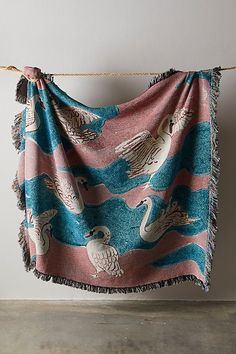 a blue and pink blanket hanging on a clothes line with two swans flying over it