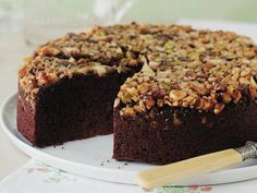 a chocolate cake with walnuts on top is sitting on a plate next to a knife