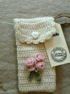 a crocheted cell phone case with pink flowers on it and a white tag