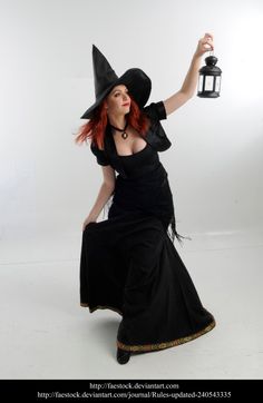 a woman dressed as a witch holding a lantern in one hand and wearing a black hat on the other