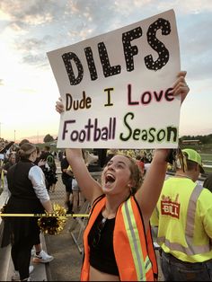 a woman holding up a sign that says dilffs dude i love football season with other people in the background