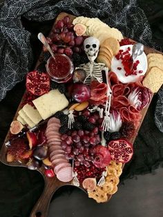 a wooden platter filled with cheese, crackers, fruit and skeleton figurines