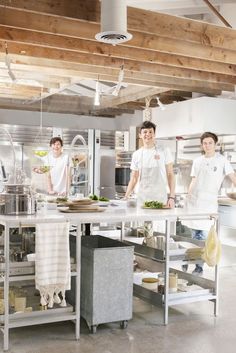 two men in white aprons standing at a kitchen island with food on it and one man behind the counter