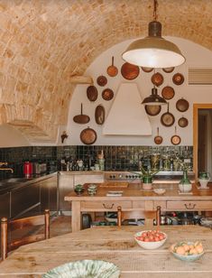 a kitchen with an arched ceiling and wooden table surrounded by bowls of fruit on the counter