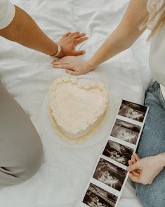 a heart shaped cake sitting on top of a table next to a couple's hands