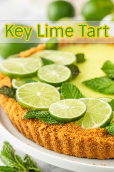 a key lime tart pie on a white plate with mint leaves and lemon wedges