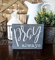 a wooden sign sitting on top of a table next to a vase and potted plant