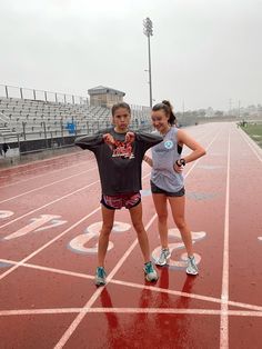 two girls standing on a track with their hands in the air