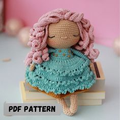 a crocheted doll sitting on top of a book with pink hair and blue dress