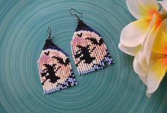 a pair of beaded earrings sitting on top of a blue plate next to a flower