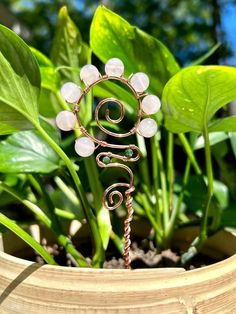 a wire sculpture sitting on top of a potted plant in front of green leaves