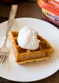 a white plate topped with waffles covered in whipped cream next to a fork