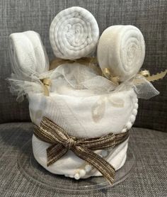 a diaper cake with three pieces of white cloth on top and gold ribbon around the edge