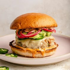 a chicken sandwich with cheese, lettuce and tomatoes on a plate next to jalapenos