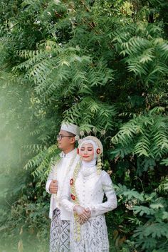 a man and woman dressed in traditional garb standing next to each other near some trees