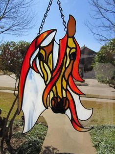 a stained glass horse head hanging from a chain in front of a tree and grass area