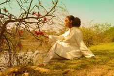 a woman sitting on the ground next to a tree with red flowers in her hands