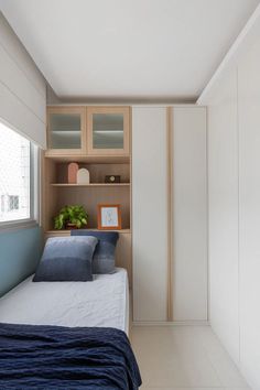 a bed sitting under a window next to a wooden shelf filled with books and plants