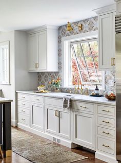 a kitchen with white cabinets and gold accents on the windowsills, along with a rug