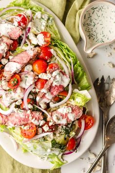 a salad with tomatoes, lettuce and dressing on it next to silverware