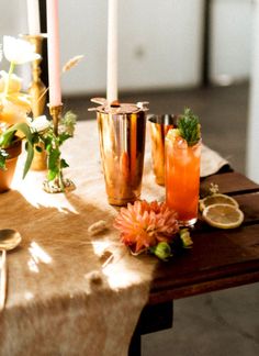 a table topped with glasses and candles next to flowers on top of a wooden table