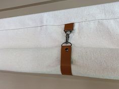 a close up of a zipper on a white pillow with a brown leather strap hanging from it