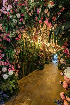 an indoor garden with lots of flowers on the walls and lights hanging from the ceiling