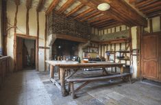 an old fashioned kitchen with a table and oven in the center, surrounded by wood beams