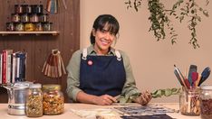 a woman sitting at a table in front of jars with plants and spices on it