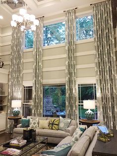 a living room filled with lots of furniture next to two large windows covered in curtains