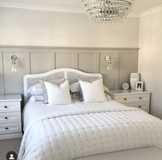 a white bed sitting in a bedroom next to a chandelier and dressers