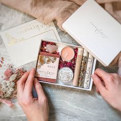 two hands are holding an open box with candles and other items in it on a marble surface