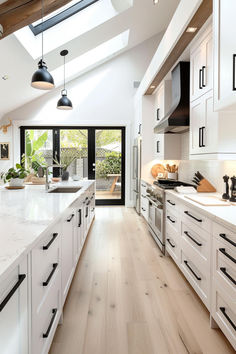 an open kitchen with white cabinets and wood flooring on the walls, along with skylights