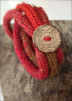 two red bracelets sitting on top of a piece of wood next to a button