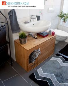 a cat sitting on top of a wooden cabinet next to a white sink and toilet