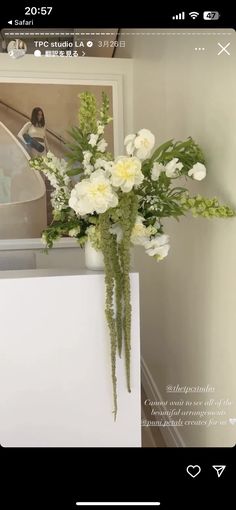 a vase filled with white flowers sitting on top of a counter next to a wall