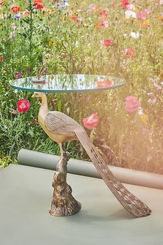 a bird statue sitting on top of a table in front of some flowers and plants