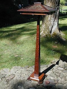 a wooden post with a lamp on it in the grass near a tree and some rocks