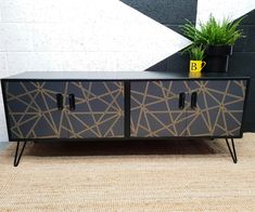 a black and gold sideboard sitting on top of a rug next to a potted plant